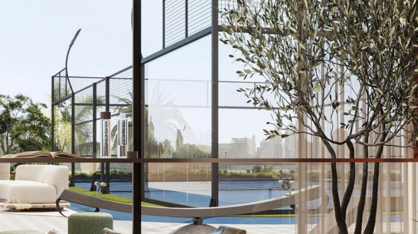 A bright, modern lounge with a white chair, hammock and potted tree inside. The large picture windows of Rabdan Gardens overlook an outdoor padel or tennis court and lush vegetation.