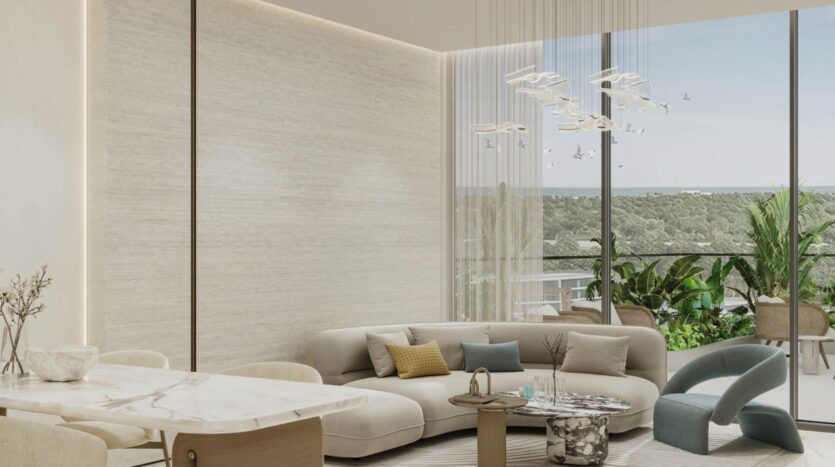 A modern living room in Rabdan Gardens with a curved beige sofa, marble dining table, contemporary chandelier, blue accent chair and large windows overlooking a balcony with green plants and panoramic views of the outdoors.