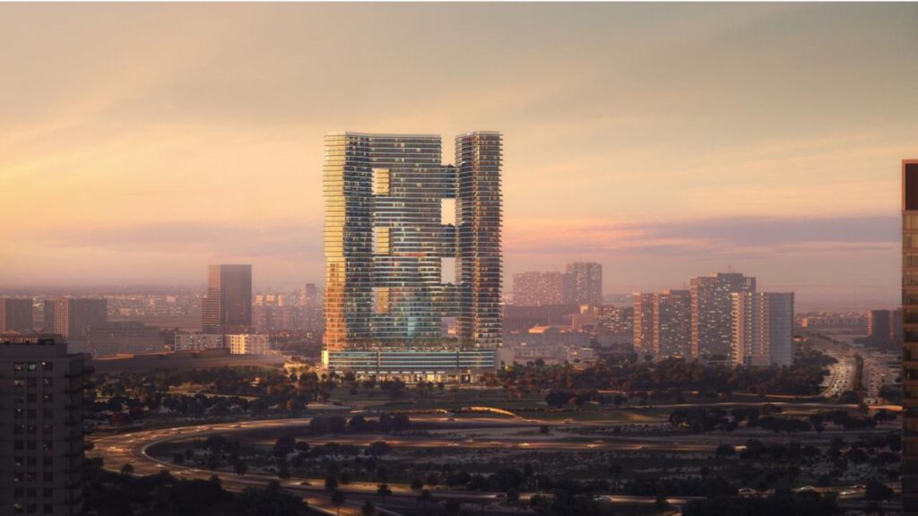 A modern skyscraper, with its rectangular cut-outs and terraces, is illuminated at dusk, among other city buildings, surrounded by winding roads and greenery, under a pastel sky.