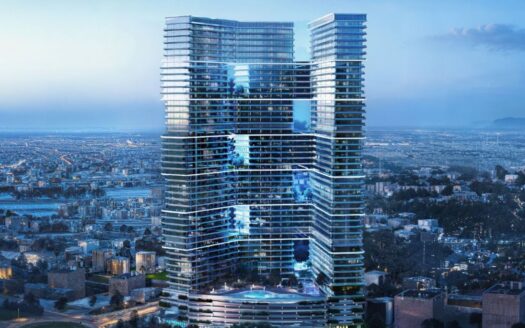 Un moderno edificio con fachadas de cristal y múltiples terrazas domina un extenso paisaje urbano al atardecer, cuando las luces comienzan a aparecer en la ciudad.