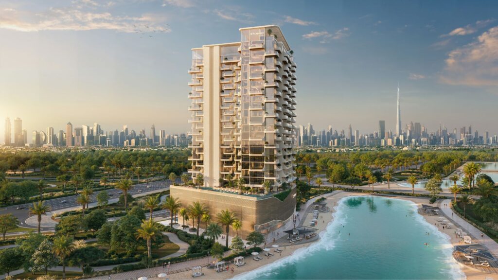 Il Caden è un moderno grattacielo residenziale situato ai margini di una laguna turchese con spiagge sabbiose, circondato da palme. Lo skyline di Dubai, compreso il Burj Khalifa, è visibile sullo sfondo in un cielo limpido.