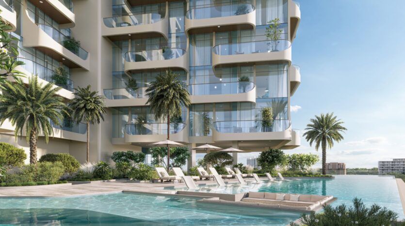 Il Caden è un moderno edificio di appartamenti con ampi balconi in vetro che si affacciano su una lussuosa piscina all'aperto, con lettini e ombrelloni, circondata da palme e vegetazione lussureggiante sotto un cielo azzurro e limpido.