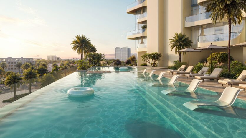 La moderna piscina a sfioro del Caden è addobbata con lettini, ombrelloni e palme in una giornata di sole accanto a un grande condominio, con vista su un paesaggio urbano di edifici e vegetazione lussureggiante sullo sfondo.