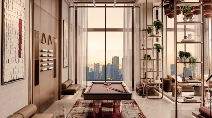 The Symphony is a modern, luxurious room with a pool table at its center, floor-to-ceiling windows with city views, elegant seating, wall art and open shelves displaying plants and decorative objects. Warm lighting creates a welcoming atmosphere.