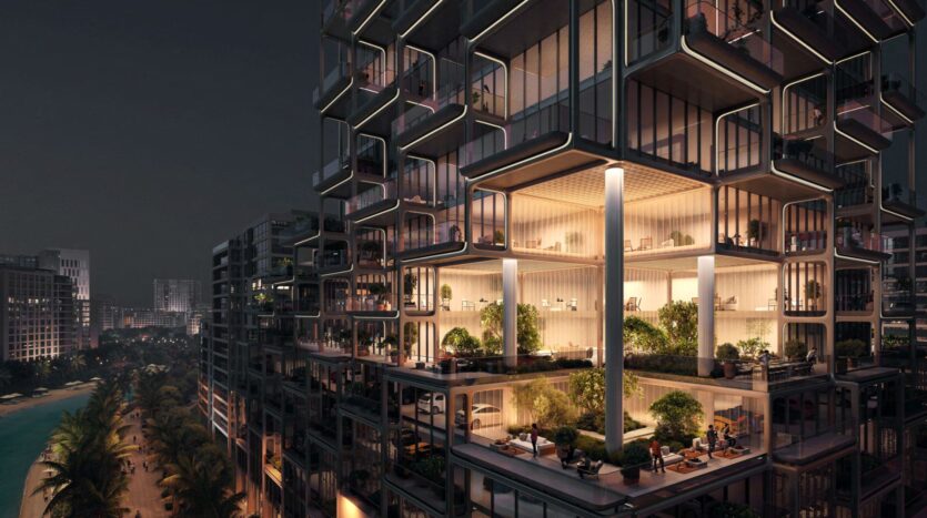 The Symphony, a modern skyscraper, sparkles at night with illuminated glass terraces offering greenery, outdoor seating and breathtaking views of the cityscape, palm trees and water below.