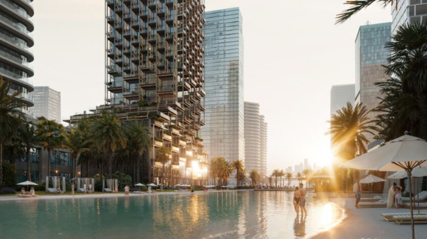 A couple strolls along the edge of a large swimming pool at sunset at The Symphony, an urban complex surrounded by modern skyscrapers, palm trees, and lounge chairs.