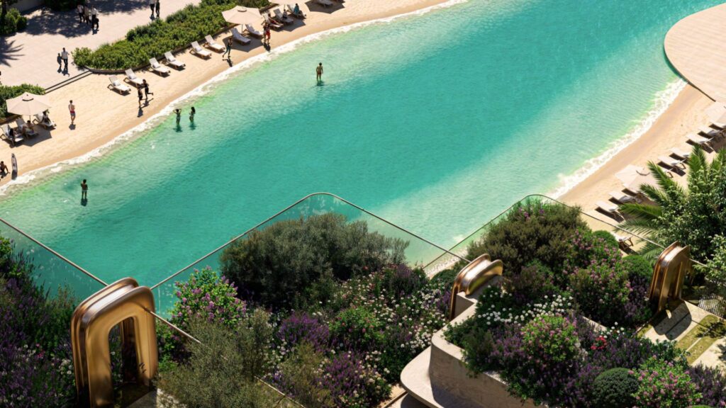 A rooftop garden with lush vegetation at Symphony overlooks a large turquoise pool, where people relax and swim near the sandy shoreline lined with sun loungers and umbrellas.