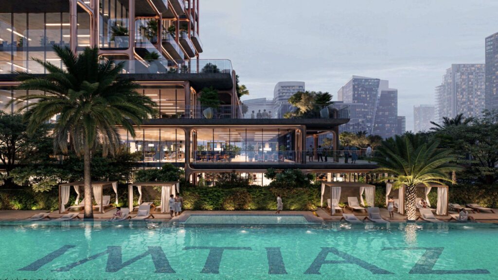 A modern, multi-storey building with large bay windows overlooks a luxurious outdoor pool, part of the Symphony residence. Palm trees, sun loungers and cabanas surround the water marked "IMTIAZ", against a backdrop of the city's skyscrapers.
