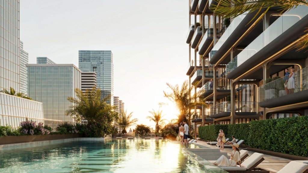 Ein moderner Außenpool namens The Symphony ist bei Sonnenuntergang von üppigen Pflanzen und eleganten Gebäuden umgeben, und die Menschen entspannen sich auf Liegestühlen am Pool und genießen die ruhige Atmosphäre.