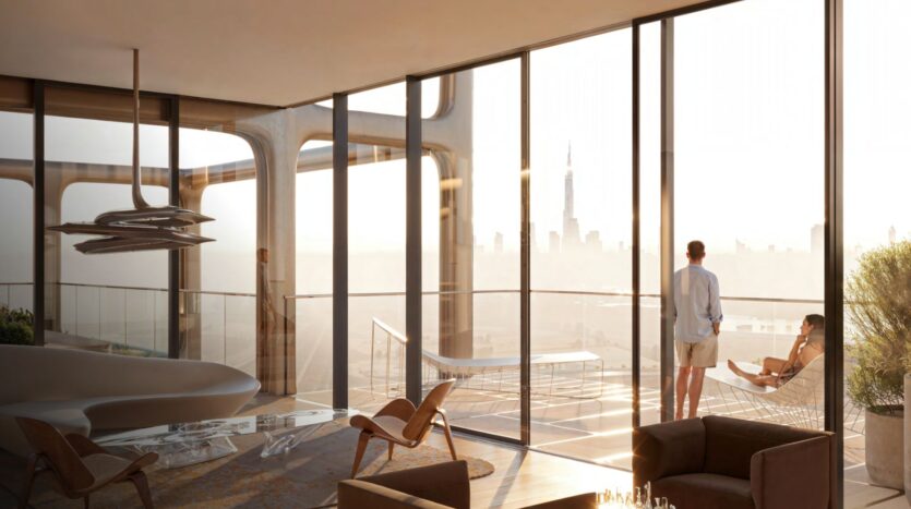 A sunny, modern apartment in The Symphony features floor-to-ceiling windows overlooking the city skyline. A man stands by the glass, while a woman relaxes on a hanging armchair on the balcony. Elegant furniture decorates the open-plan living space.