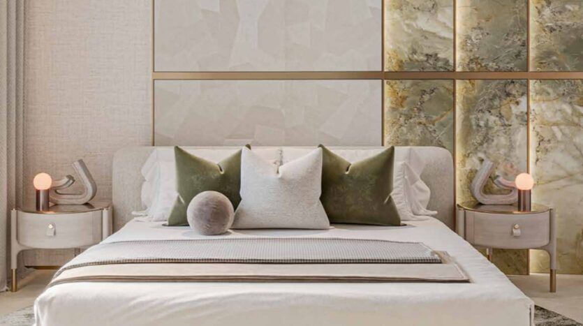 A modern bedroom in Arlington Park with a white linen bed, three large pillows in white and olive green, a round gray cushion, two nightstands with lamps, and a marble wall behind the headboard.