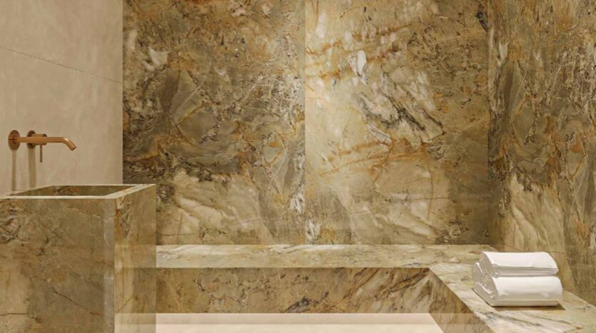 A modern bathroom in Arlington Park 2 with tan and gold marble walls, a matching marble sink with a bronze faucet, and a marble bench topped with two neatly folded white towels.