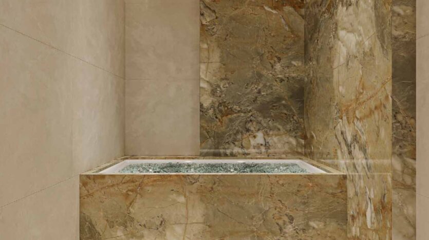 A modern indoor stone hot tub with clear water, surrounded by beige and brown marble tiles on the walls and outside of the tub, adds a touch of Arlington Park 2 luxury to your home.