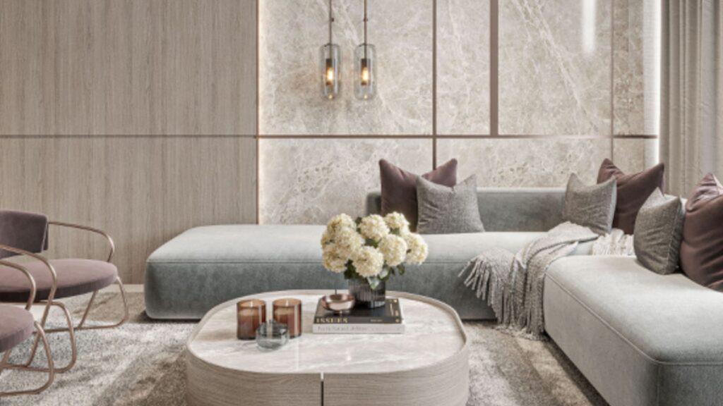 Salotto moderno con divano componibile grigio chiaro, accenti murali in marmo e tappeto Floarea Breeze. Un tavolino rotondo in marmo ospita fiori e libri, mentre morbide coperte, candele e lampade a sospensione contemporanee completano il look.