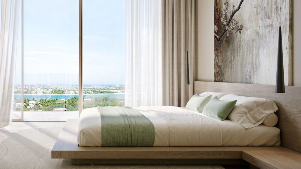 A modern bedroom with a low wooden bed, green and white bedding, soft natural light, large floor-to-ceiling windows, sheer curtains, and a picturesque view of the water and greenery outside create a soothing, hado-inspired retreat.