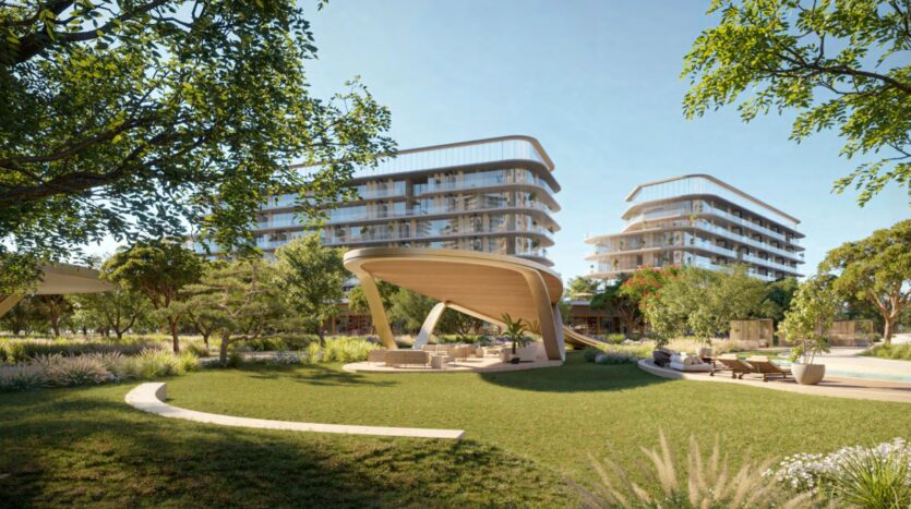 A modern outdoor lounge with a curved wooden canopy by Hado sits amid greenery, framed by two contemporary glass-clad residential buildings and a vibrant blue sky in the background.