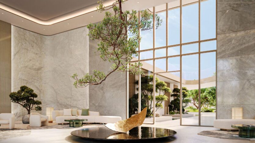 A spacious and elegant entrance hall with marble walls, large floor-to-ceiling windows, a modern circular water feature inspired by Hado with a tree and a gold sculpture, and minimalist white seating with greenery throughout the establishment.