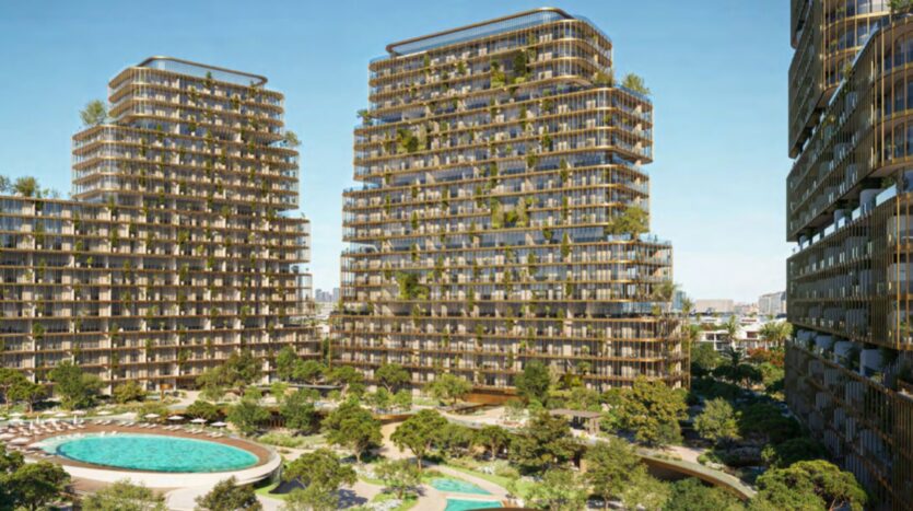 Three modern Hado towers with glass facades and balconies covered in greenery, surrounded by lush gardens, trees, and swimming pools under a clear blue sky.