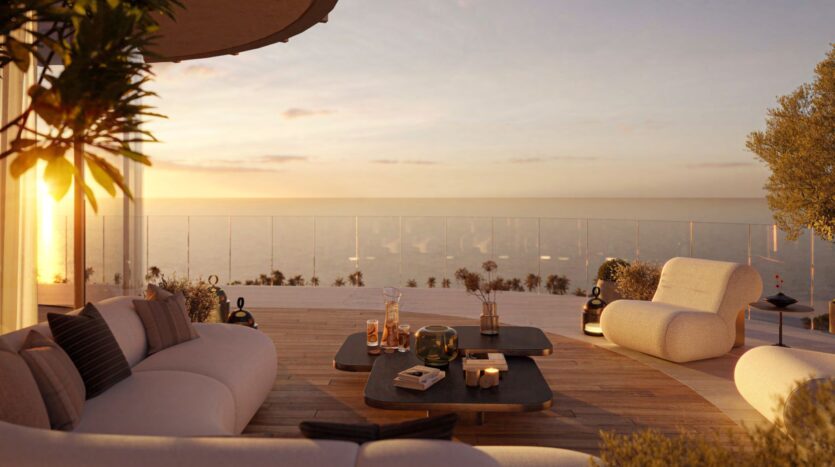 Modern outdoor terrace with stylish sofas and coffee tables, overlooking the calm sea at sunset. Warm sunlight, a Hado-inspired glass balustrade, and minimalist décor create a relaxing and luxurious atmosphere.