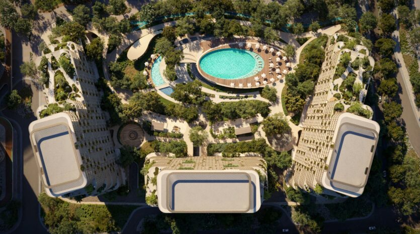 Aerial view of a modern, landscaped Hado complex consisting of three uniquely shaped buildings surrounding an oval pool, lounge chairs, and lush green walkways. Roads and trees line the property.