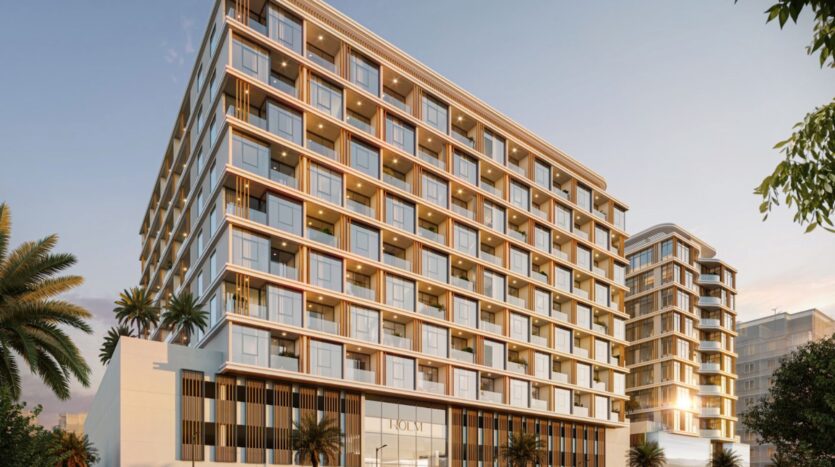 Holm One, a modern multi-story building, features large bay windows and balconies surrounded by palm trees under a clear sunset sky. The sleek, contemporary design is enhanced by warm interior lighting.