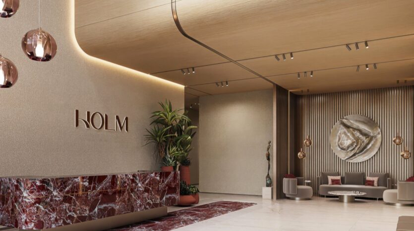 A modern entrance hall with beige walls, a marble reception desk, large potted plants, hanging lamps, and "Holm One" on the wall. At the back, a seating area with gray sofas and abstract wall art.