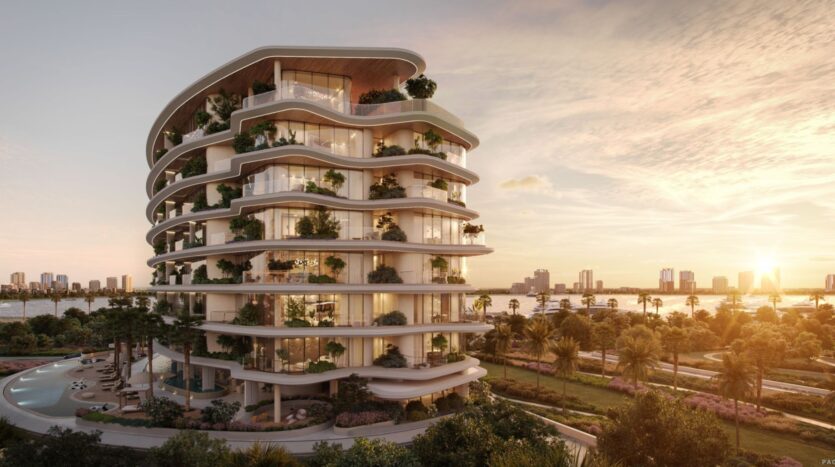 A modern multi-story building constructed by Lia features curved balconies filled with greenery, overlooking a waterfront at sunset. Palm trees and landscaped gardens surround the structure, with the city skyline in the background.