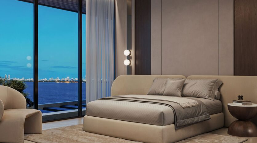Modern bedroom with a large bed, beige furniture, and a round side table by Lia, featuring floor-to-ceiling windows overlooking the city skyline and water at dusk. Soft lighting and neutral tones create a calm atmosphere.
