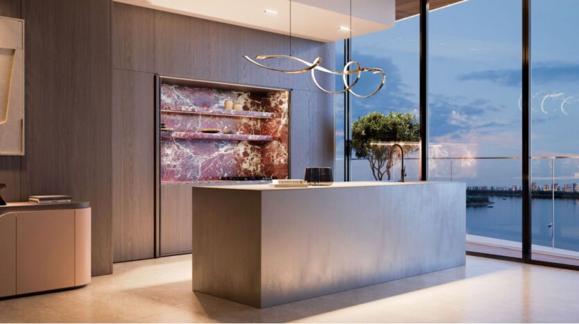 Modern kitchen with minimalist island, sculptural pendant lights, and marble backsplash. Large floor-to-ceiling windows offer breathtaking views of the water and Lia's urban landscape at sunset. A small potted tree decorates the island.