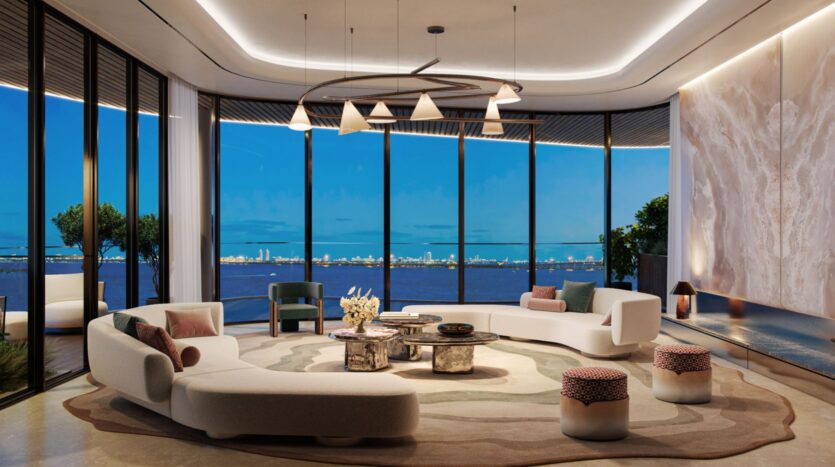 The modern and luxurious living room designed by Lia features curved white sofas, round coffee tables, and floor-to-ceiling windows that offer breathtaking views of the ocean and the city at dusk. Soft lighting and elegant décor complete the space.