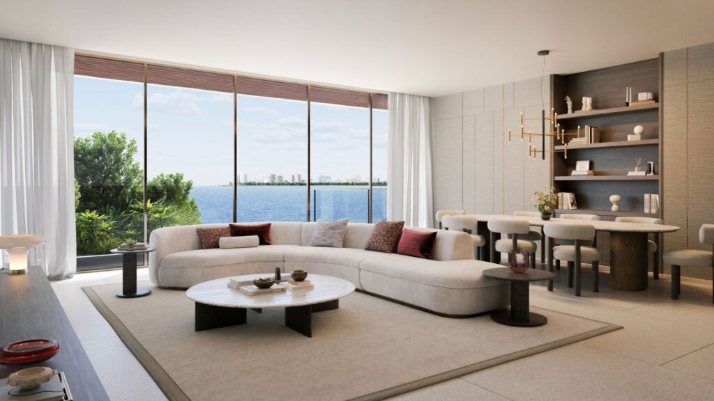 Modern living and dining room with a curved white Lia sofa, round coffee table, and shelves. Large windows offer views of the water and skyline; natural light fills the space, complemented by neutral tones and elegant décor.