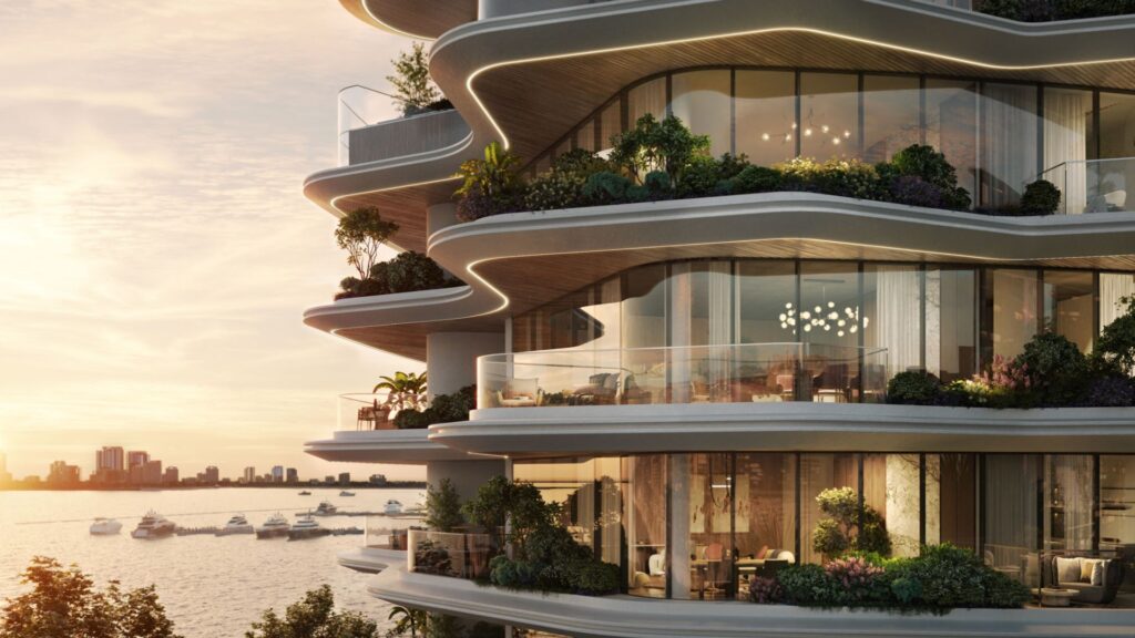 Das moderne Luxus-Apartmentgebäude Lia mit seinen geschwungenen, üppig begrünten Balkonen bietet einen Blick auf eine ruhige Küste mit Yachten und eine atemberaubende Skyline der Stadt bei Sonnenuntergang.