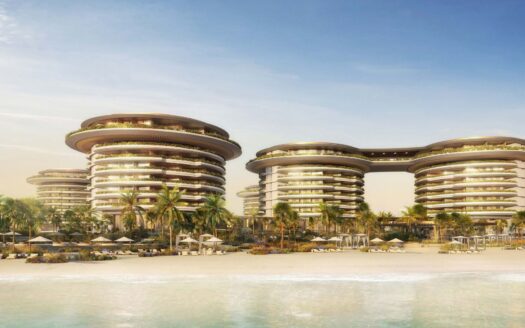 The futuristic seaside resort The Edition consists of circular multi-story buildings surrounded by palm trees and sun loungers on a sandy beach, facing calm blue water under a clear sky.