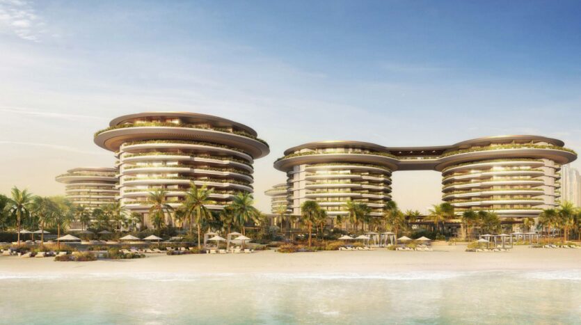 The futuristic seaside resort The Edition consists of circular multi-story buildings surrounded by palm trees and sun loungers on a sandy beach, facing calm blue water under a clear sky.