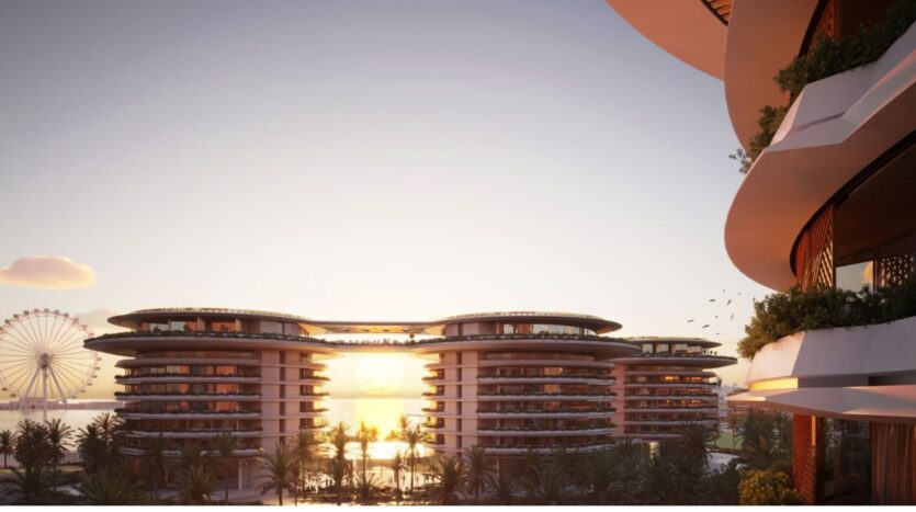 Sunset view of the modern, circular buildings with balconies at The Edition, framed by palm trees and a Ferris wheel in the distance, creating a tranquil, upscale coastal atmosphere.