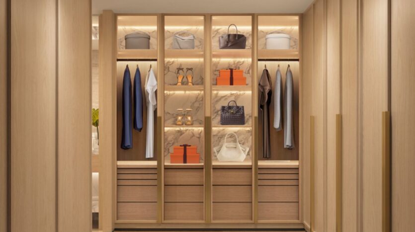 The modern dressing room at The Edition features light wood shelves, drawers, and backlit marble accents. Clothes, handbags, shoes, and signature orange boxes are neatly hung, giving the space a clean, organized, and luxurious look.