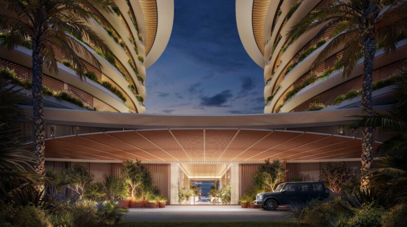 The entrance to a modern luxury hotel at dusk, framed by curved balconies with lush greenery and palm trees, is illuminated by warm light next to a parked car. The open design of the Edition offers breathtaking views of the ocean.