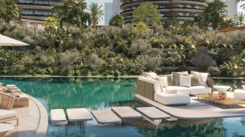 The Edition's luxurious outdoor pool with floating stone steps leading to a lounge area with white sofas and cushions; lush greenery and modern buildings in the background under a clear sky.