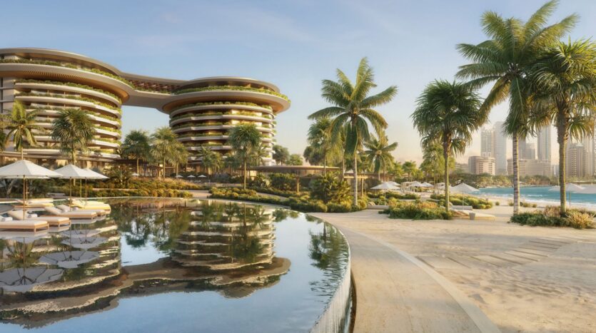 The Edition is a luxury beach resort with modern curved buildings, palm trees, lounge chairs, and umbrellas by a reflective pool, overlooking a sandy beach and the city skyline in the background under a clear sky.