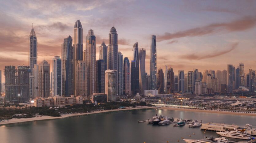 A panoramic view of a modern city skyline at sunset, with The Edition standing among tall skyscrapers, overlooking a marina filled with yachts and calm water, all under a soft pink and orange sky.