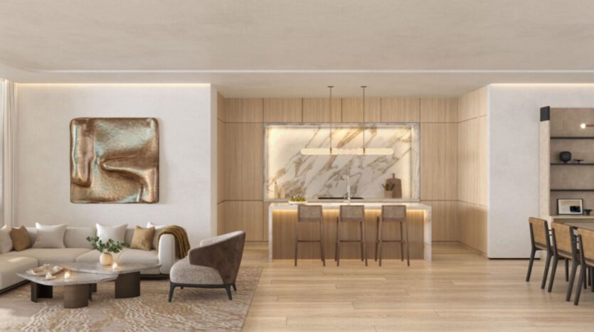 The modern, open living space at The Edition hotel features a beige sectional sofa, abstract wall art, a marble kitchen island with bar stools and a dining area, all accented by light wood finishes and neutral tones.
