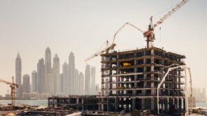 Ein mehrstöckiges Gebäude im Bau mit Kränen und Gerüsten vor dem Hintergrund der Skyline verdeutlicht, warum neue Immobilien inmitten von hohen Wolkenkratzern und einem nebligen Himmel im Hintergrund für Investoren so attraktiv sind.
