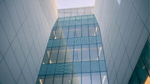 Modernes Gebäude mit schlichten weißen Wänden und großen blau getönten Fenstern, von unten gesehen – vor dem Hintergrund des klaren Himmels wird die architektonische Innovation hervorgehoben, die Investitionen in Dubai zu einer attraktiven Wahl macht.