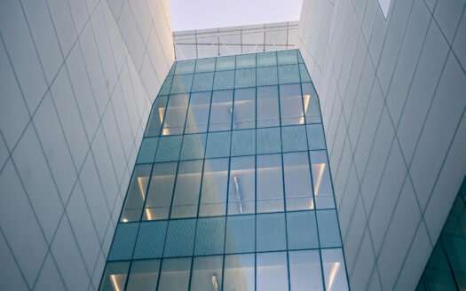 Bâtiment moderne aux murs blancs épurés et aux grandes baies vitrées teintées de bleu, vu d'en bas - mettant en valeur l'innovation architecturale qui fait d'investir à Dubaï un choix séduisant sur fond de ciel clair.