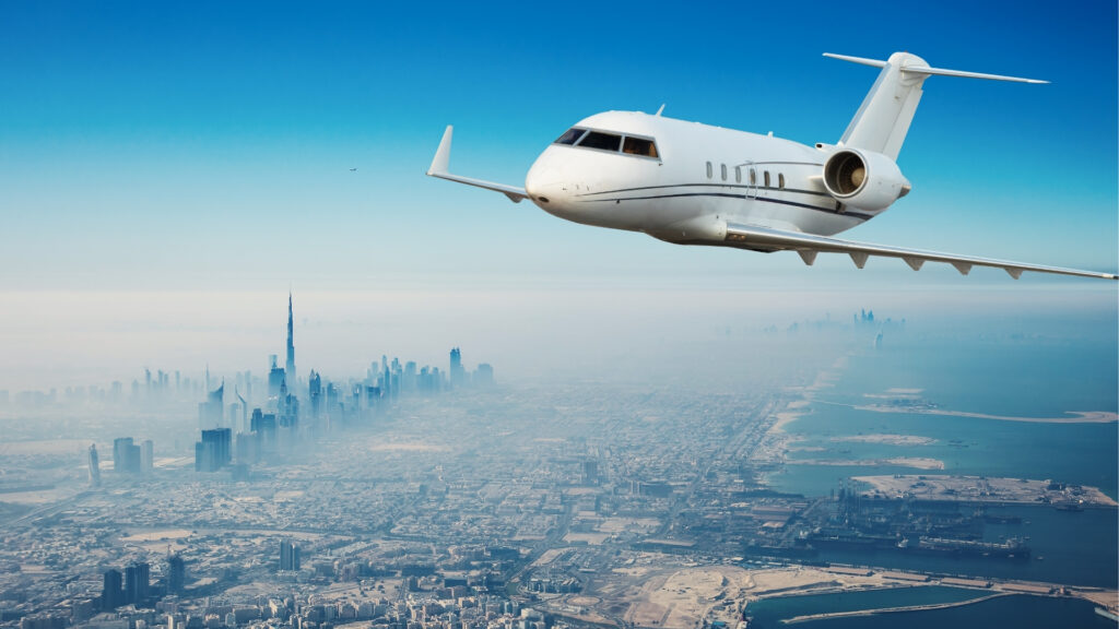Un jet privado blanco sobrevuela el moderno paisaje urbano de Dubái, con rascacielos como el Burj Khalifa y la costa a sus pies, bajo un cielo azul claro, una escena muy apreciada por los millonarios.