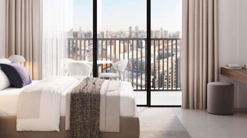 Modern room at Alta View with a well-made bed, large windows and curtains, a balcony table with chairs, and breathtaking views of the city skyline. Neutral tones and minimalist decor create a calm atmosphere.