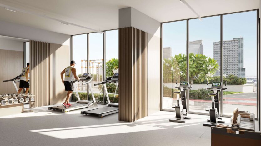 A man runs on a treadmill in Alta View's modern, brightly lit gym, which features large windows, weight machines, and exercise bikes. The city's buildings and greenery are visible outside.