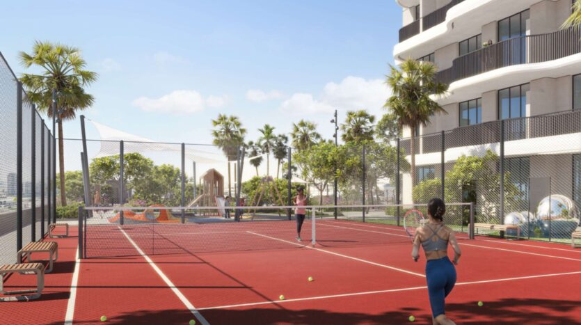 Two people are playing tennis on an outdoor red court at Alta View, surrounded by palm trees and modern buildings. A playground and benches are visible nearby, under a clear blue sky.