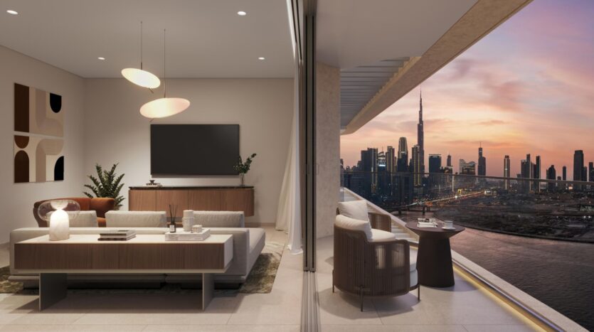 The modern living room in neutral tones opens onto a balcony overlooking the city at sunset, with skyscrapers and the Burj Khalifa. The interior space showcases art with an elegant sofa, artwork, a television, plants, and hanging lamps.