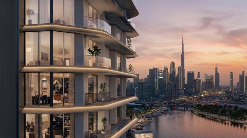 A modern tower with glass balconies showcases architectural artistry as it overlooks a marina and river at sunset, with the city skyline and Burj Khalifa visible in the background. Warm lights shine inside the apartments.